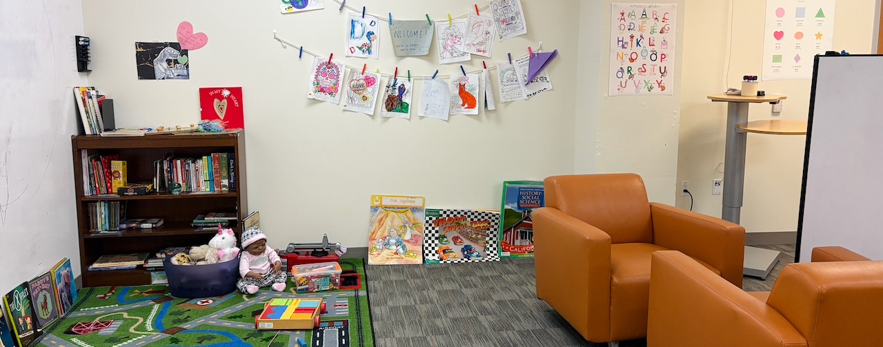 A bright room with armchairs, a bookshelf, a colorful rug, and drawings on the wall