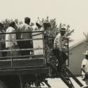 Men in work clothes and hats climb down from the back of a truck in a black-and-white photo