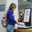 A student in a purple sweatshirt scans a library book to check out