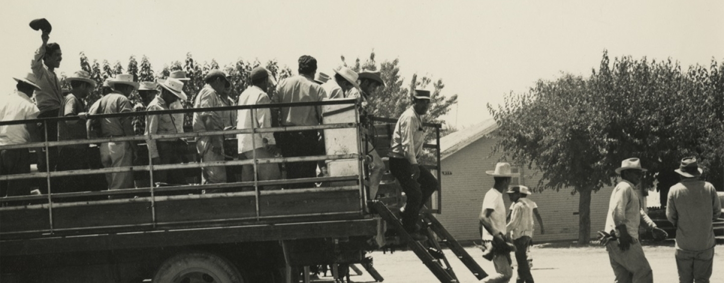 Men in work clothes and hats climb down from the back of a truck in a black-and-white photo