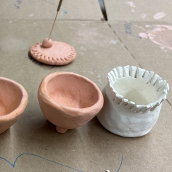 Small handmade clay pots and sculptures on cardboard