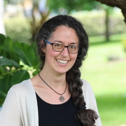 A smiling person with a long braid and glasses sitting outdoors