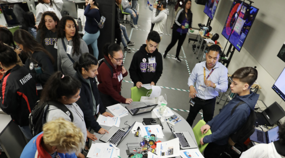 A crowd of people working on laptops and using VR equipment