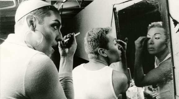 Two people sharing mirror for applying make-up