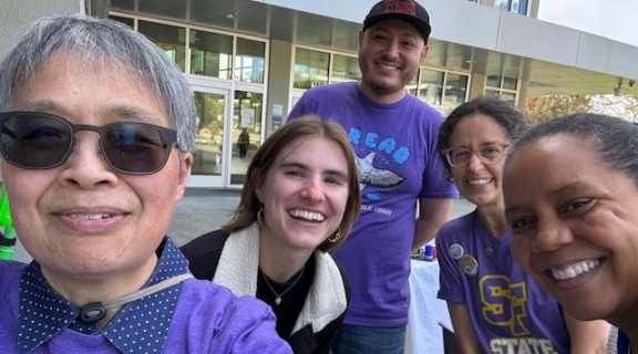 Five smiling people clustered together for a selfie